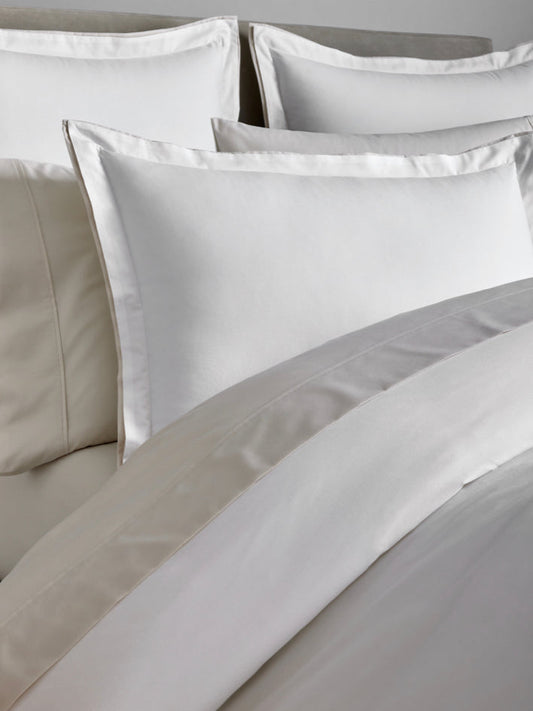 A bed dressed with a duvet in Signature White/Balinese Pearl colors and several pillows at the headboard. - {{Signature White/Balinese Pearl}}