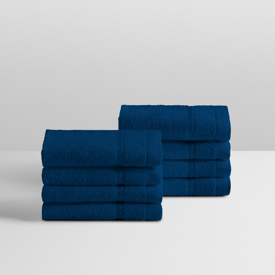 A stack of eight soft, “Riviera Navy” colored bath wash cloth neatly folded on a white surface. - {{Riviera Navy}}