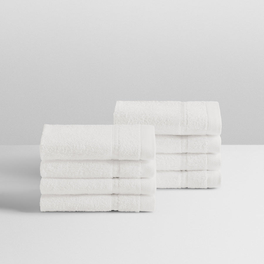 A stack of eight soft, “Signature White” colored bath wash cloths neatly folded on a white surface. - {{Signature White}}
