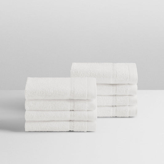 A stack of eight soft, “Signature White” colored bath wash cloths neatly folded on a white surface. - {{Signature White}}
