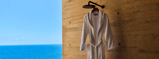 Signature cotton bathrobe with Four Seasons logo hanging under an outdoor shower by the sea