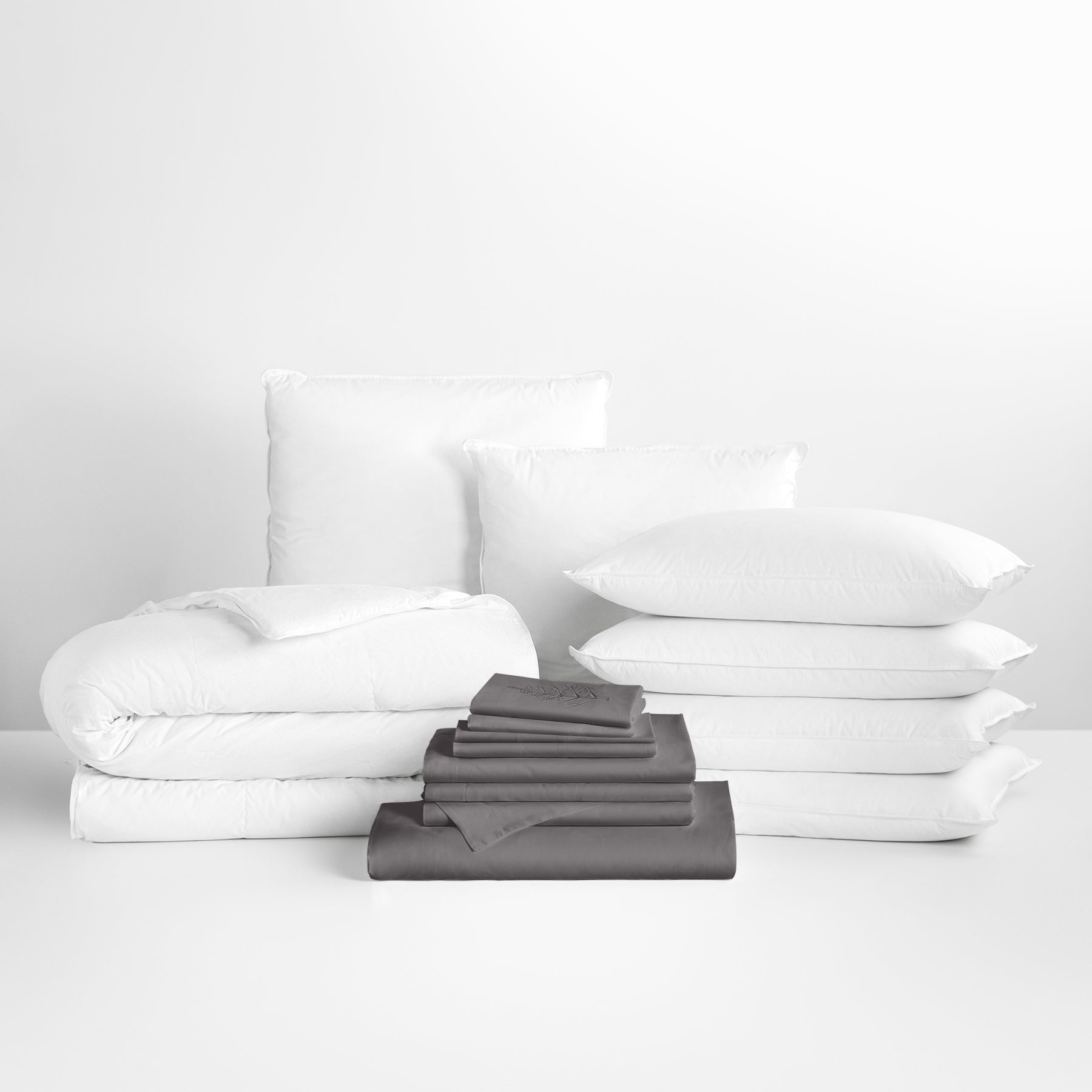 A bed dressed in a gray and white bedding set. A fluffy duvet covers the bed and pillows are stacked at the headboard, creating a neat and inviting composition. - {{Hampshire Charcoal}}