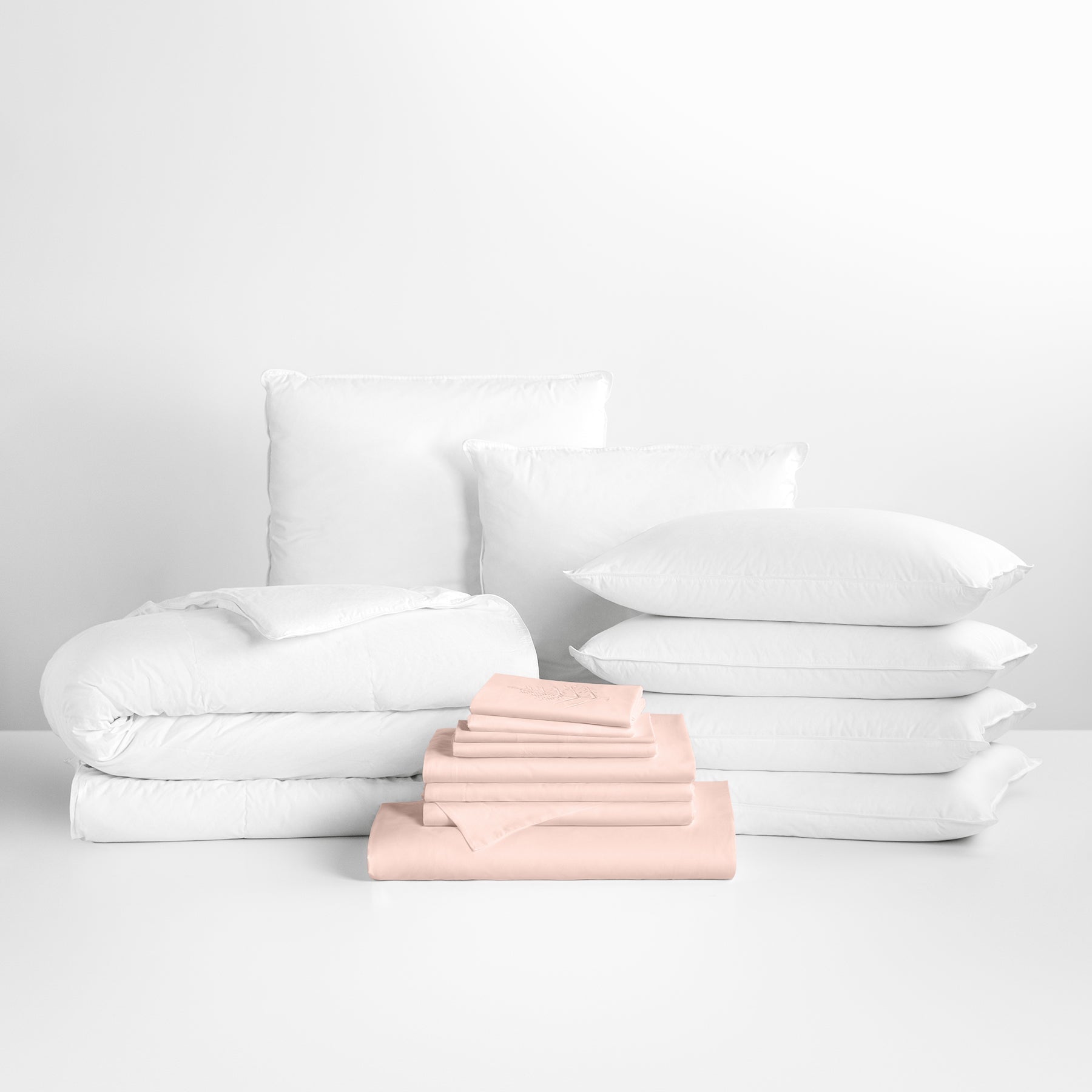 Kyoto Blush-colored sheet set in the foreground, with stacked pillows and a neatly folded duvet in the background. - {{Kyoto Blush}}