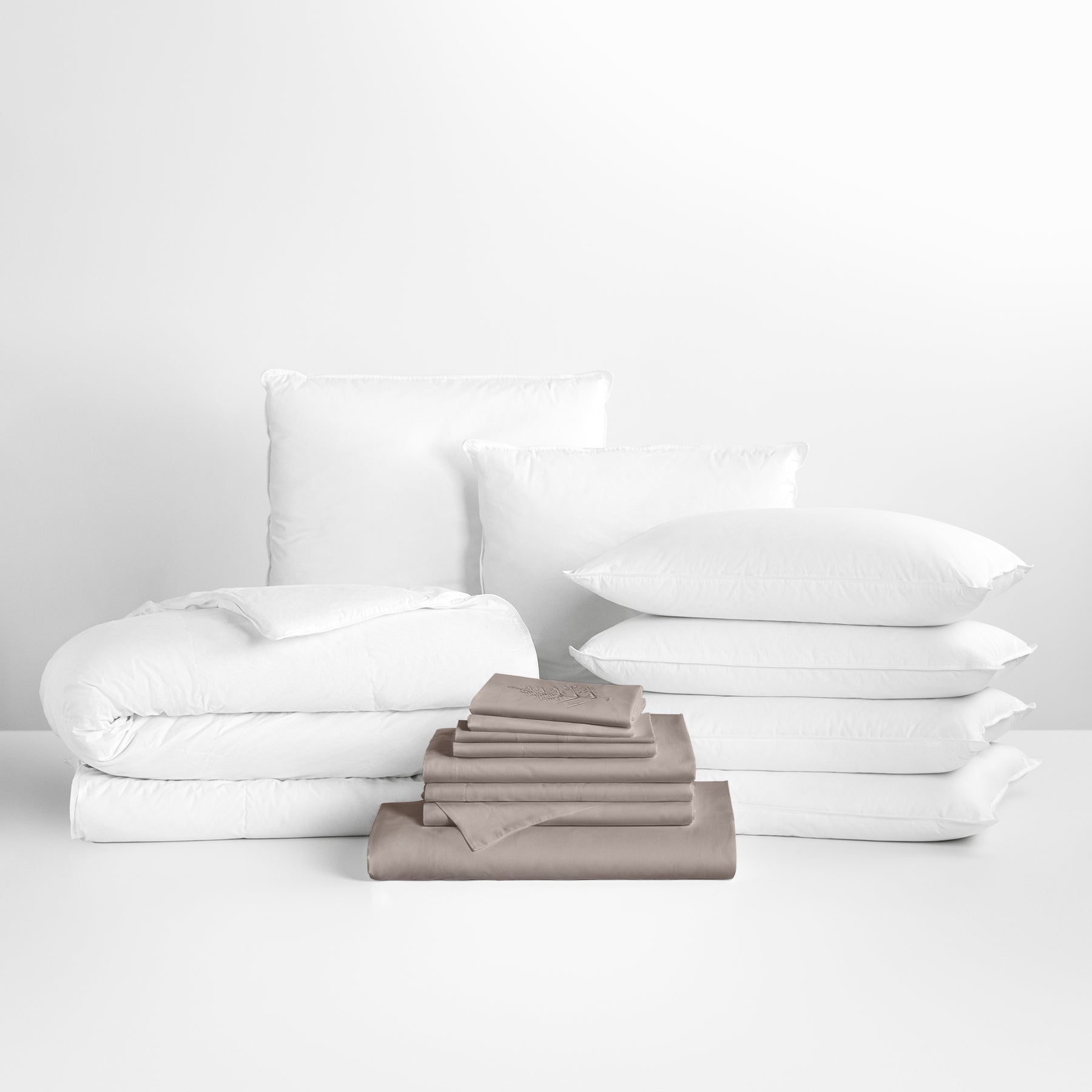 Sheet set in Moroccan Sand color in the foreground, with stacked pillows and a neatly folded comforter in the background. - {{Moroccan Sand}}