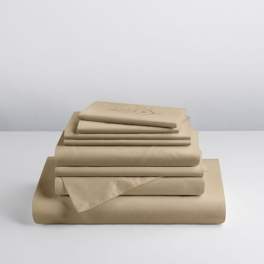 Stacked Hotel Linen Set in Egyptian Camel — folded duvet, sheets and shams; top sham shows store logo embroidery. {{Egyptian Camel}}