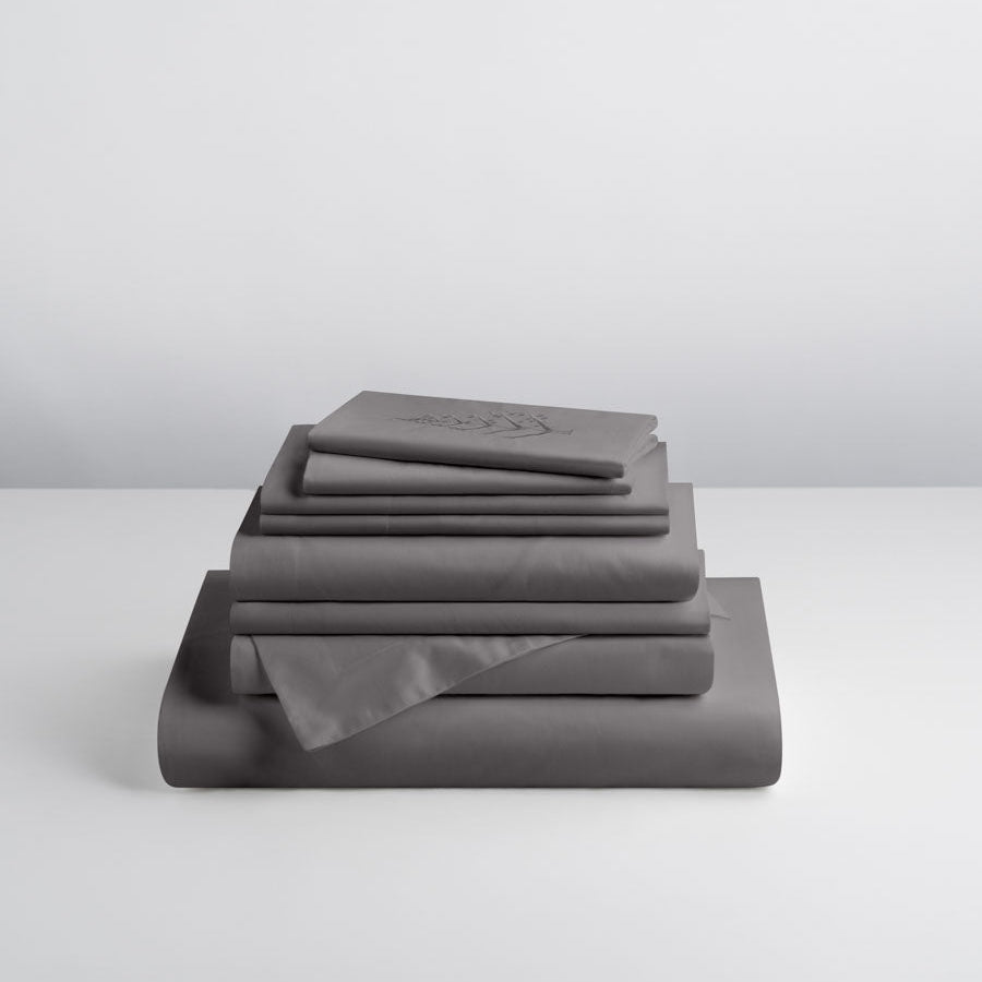 Stacked Signature Hotel Linen Set in Hampshire Charcoal, including duvet cover, sheets, and pillowcases; top piece shows subtle store logo embroidery. {{Hampshire Charcoal}}