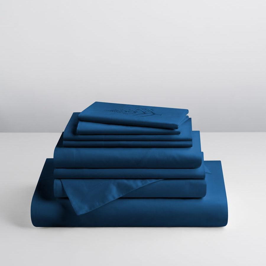 Riviera Navy linen set stacked: folded duvet and shams; top piece with tone-on-tone logo store embroidery, fitted and flat sheet. {{Riviera Navy}}