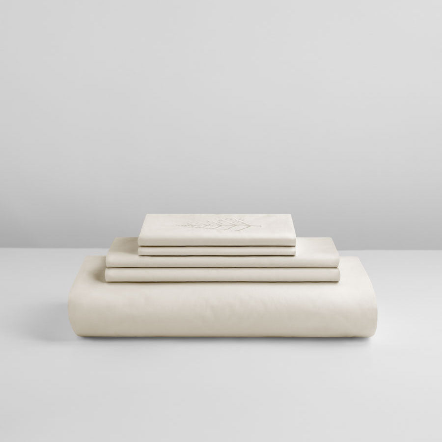 Stacked Signature Hotel Linen Set in Balinese Pearl color with folded sheets and embroidered store logo. {{Balinese Pearl}}