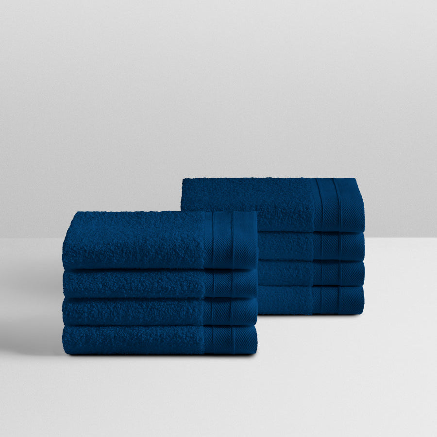 A stack of eight soft, “Riviera Navy” colored bath wash cloth neatly folded on a white surface. - {{Riviera Navy}}