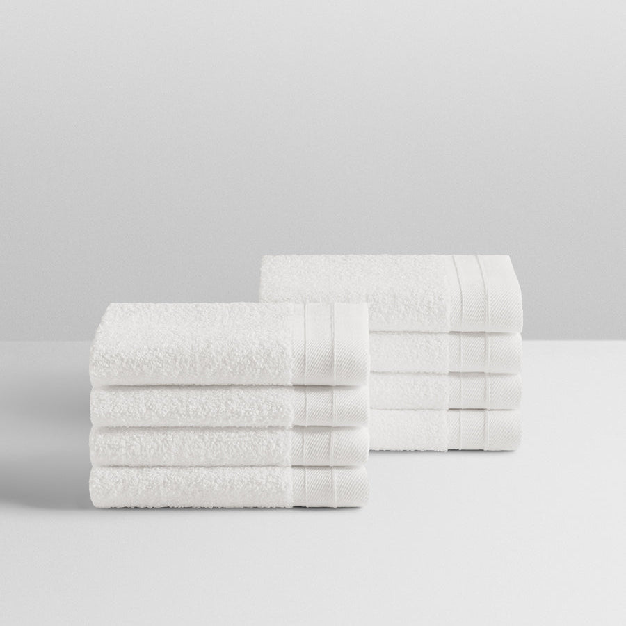 A stack of eight soft, “Signature White” colored bath wash clothes neatly folded on a white surface. - {{Signature White}}