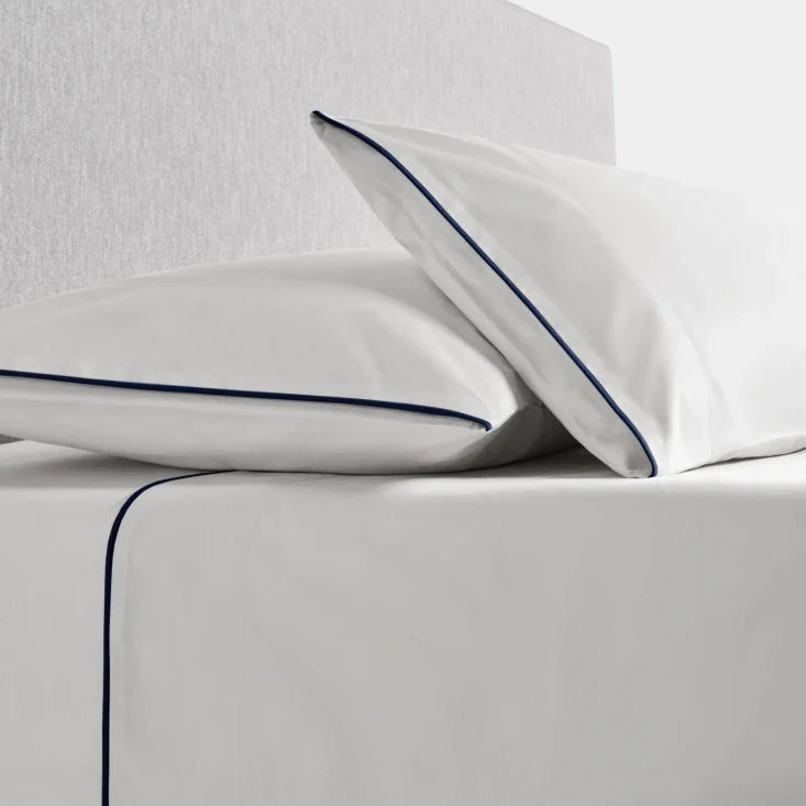 Sycamore Sheet Set in Signature White —flat and fitted sheet with modern piped hem, styled on bed with matching pillowcases. - {{Signature White}}