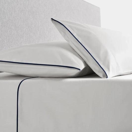 Sycamore Sheet Set in Signature White —flat and fitted sheet with modern piped hem, styled on bed with matching pillowcases. - {{Signature White}}