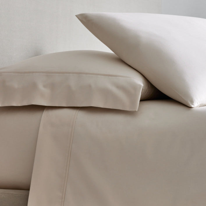 A bed with sheets and two pillows in Balinese Pearl color. - {{Balinese Pearl}}