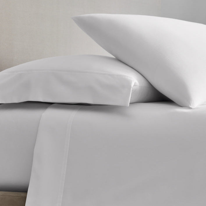 A bed with sheets and two pillows in Signature White color. - {{Signature White}}