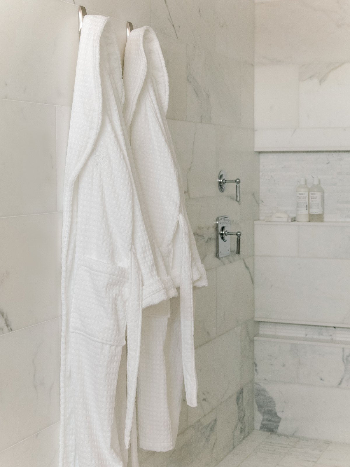 Two white bathrobes, hanging in a luxury bathroom. Soft and absorbent texture.