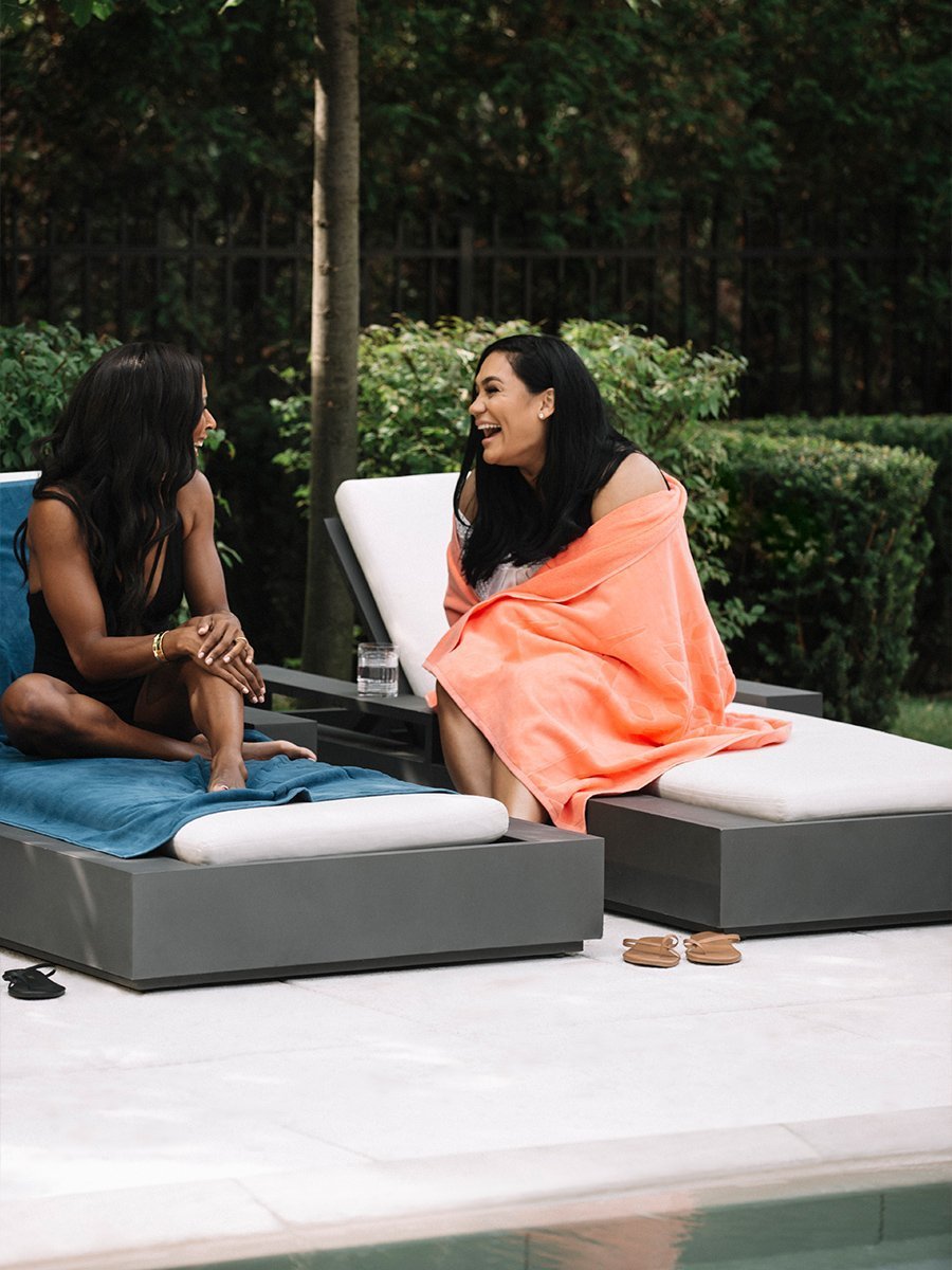 Two women are sitting outdoors, enjoying the sunshine while using Four Seasons beach towels.