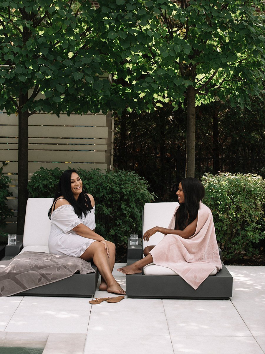 Two women are sitting outdoors, enjoying the sunshine while using Four Seasons beach towels.