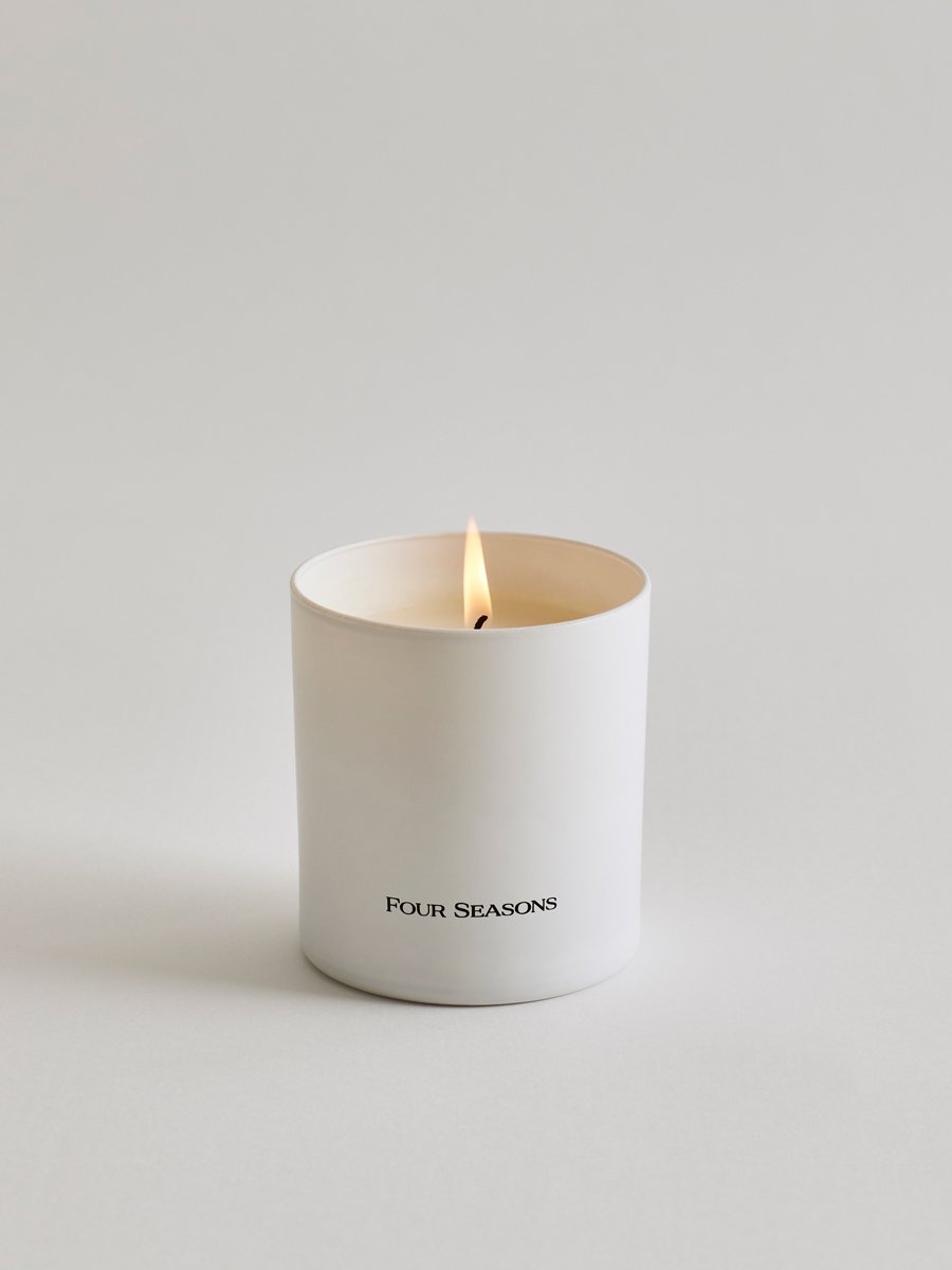 A lit Four Seasons Signature Votive - Champagne Wonderland candle, creating a warm and inviting ambiance.