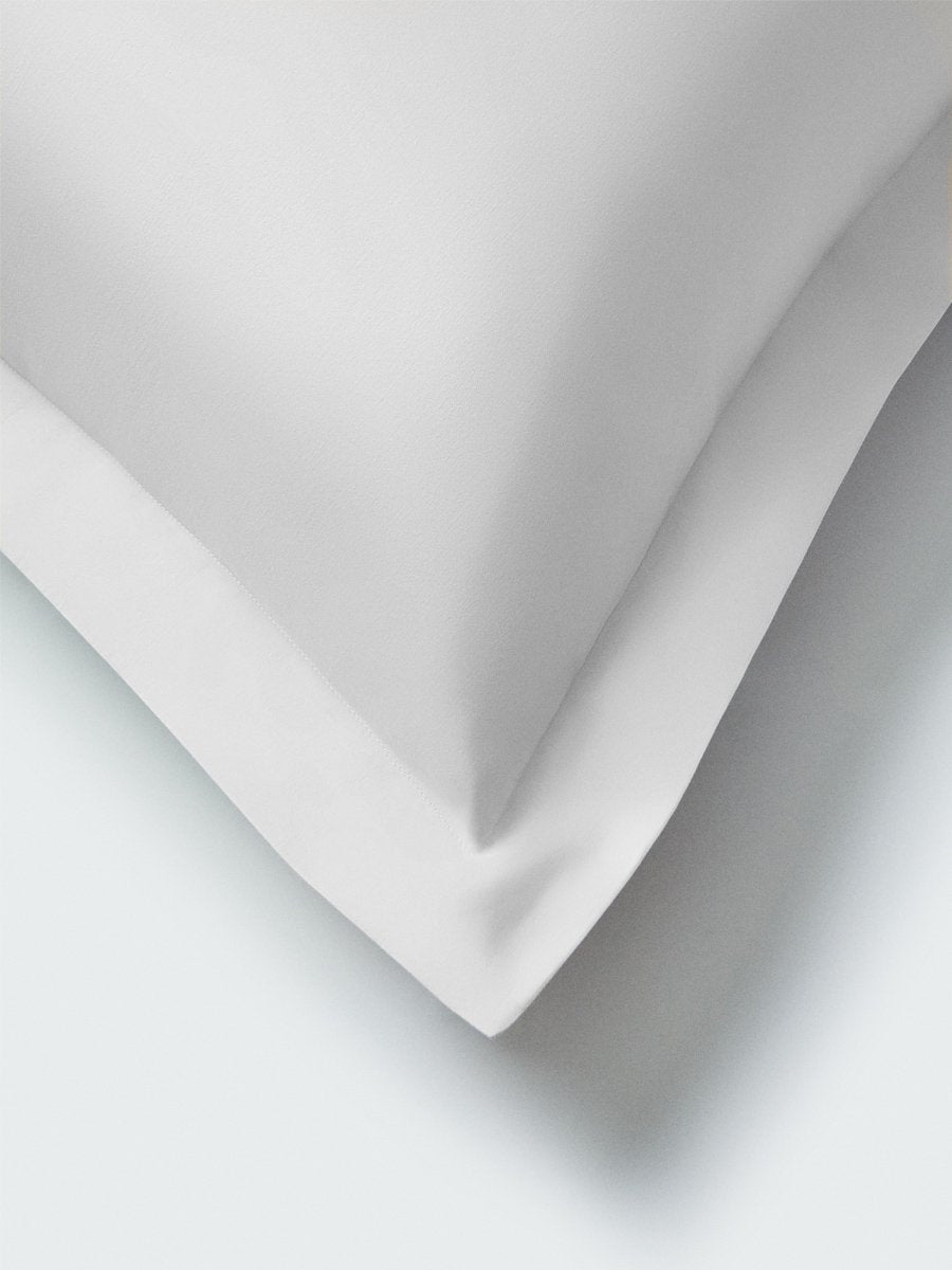 Part of a pillow with a Signature White color pillowcase featuring embroidery along the edge.