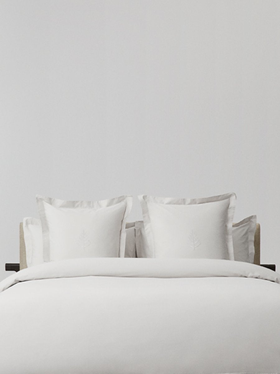 White pillows with decorative embroidery on a duvet, placed on top of a luxury bed.