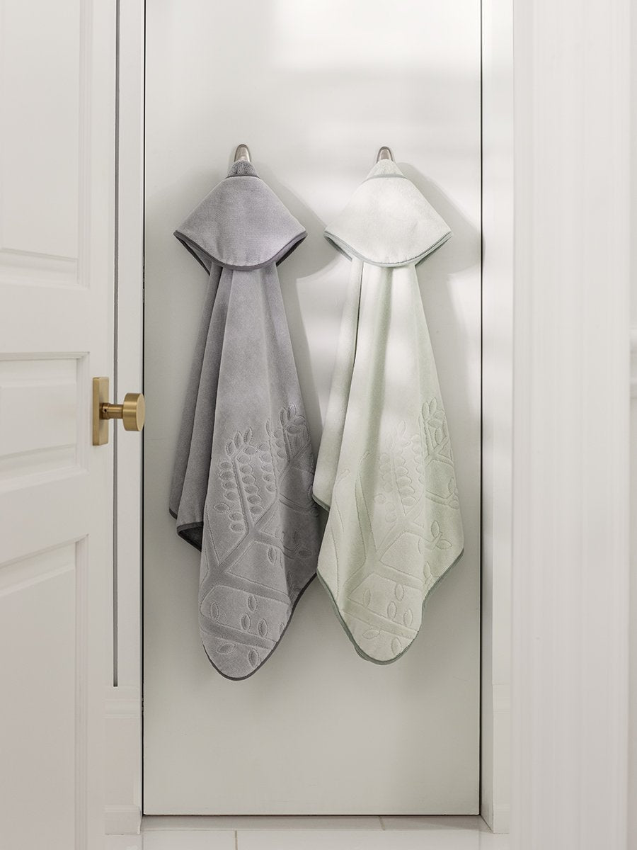 Two children's hooded towels, one in "Safari Sage" and one in "Mountain Grey", hanging on a door hook.