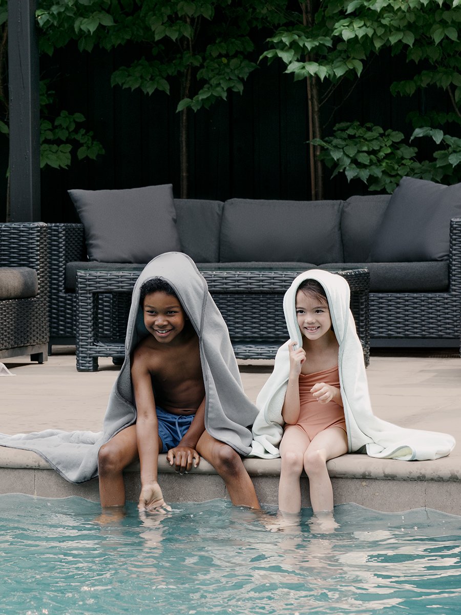 Two children splashing in a pool, each wearing a  hooded towel.