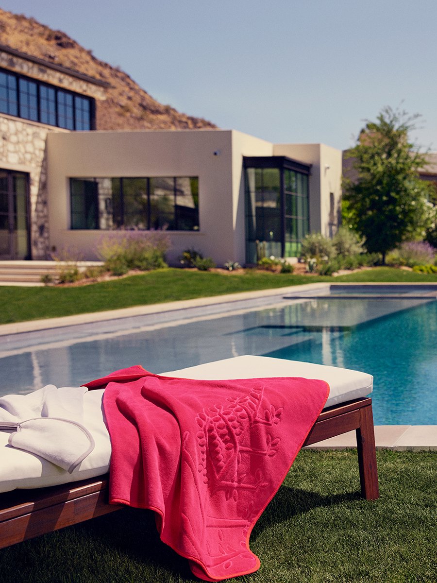 A hooded towel folded on a lounge chair by a swimming pool.