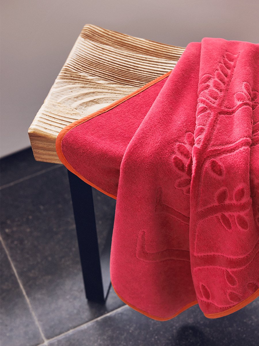 An "Coral Reef Pink" hooded towel folded on a wooden bench in a bathroom.